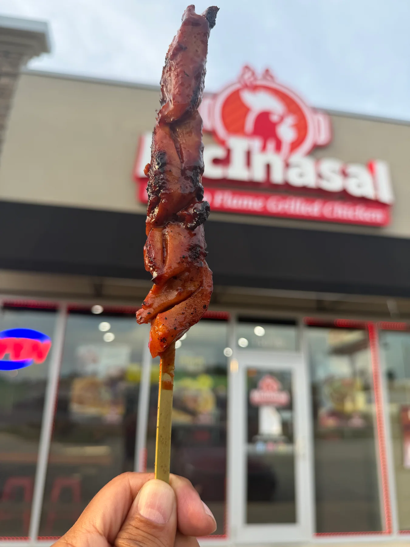 A flame-grilled chicken BBQ skewer held in front of the McInasal restaurant in Springfield